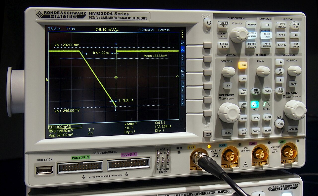 A digital oscilloscope on a bench with a bright waveform traced across its screen.
